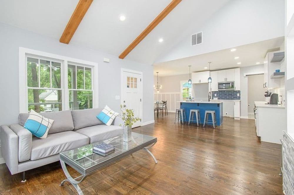 Modern living room with high ceilings, beams, and a stylish open kitchen in a bright home.