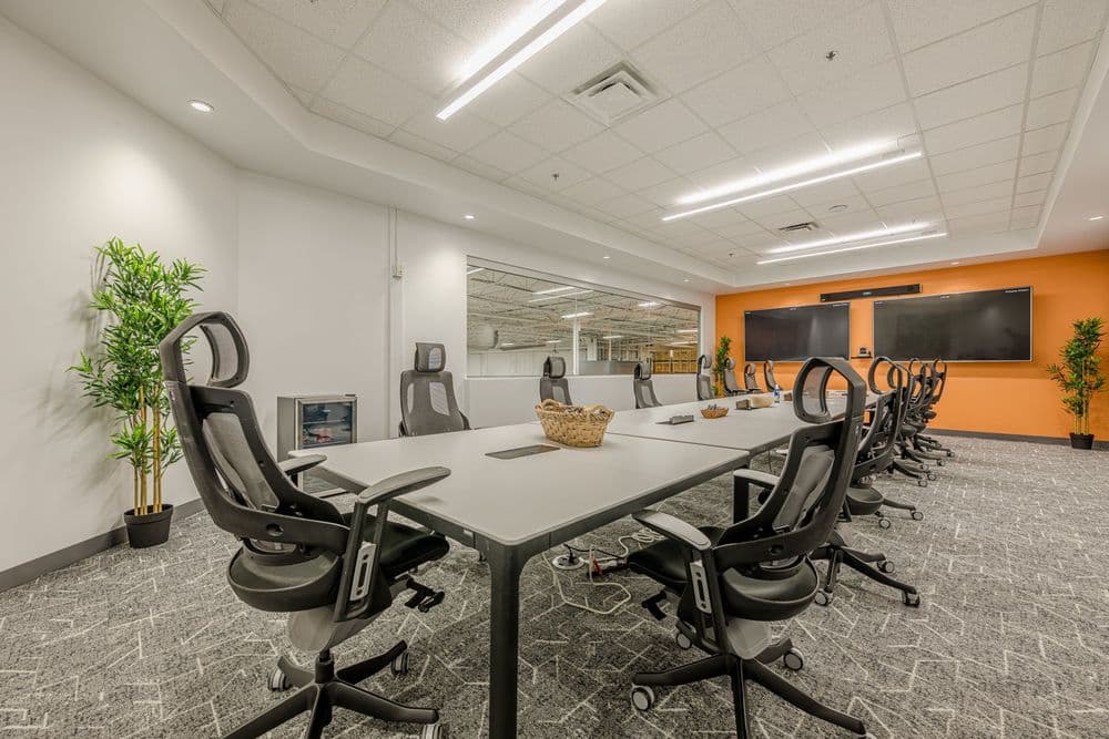 Modern conference room with large table, ergonomic chairs, and orange accent wall.