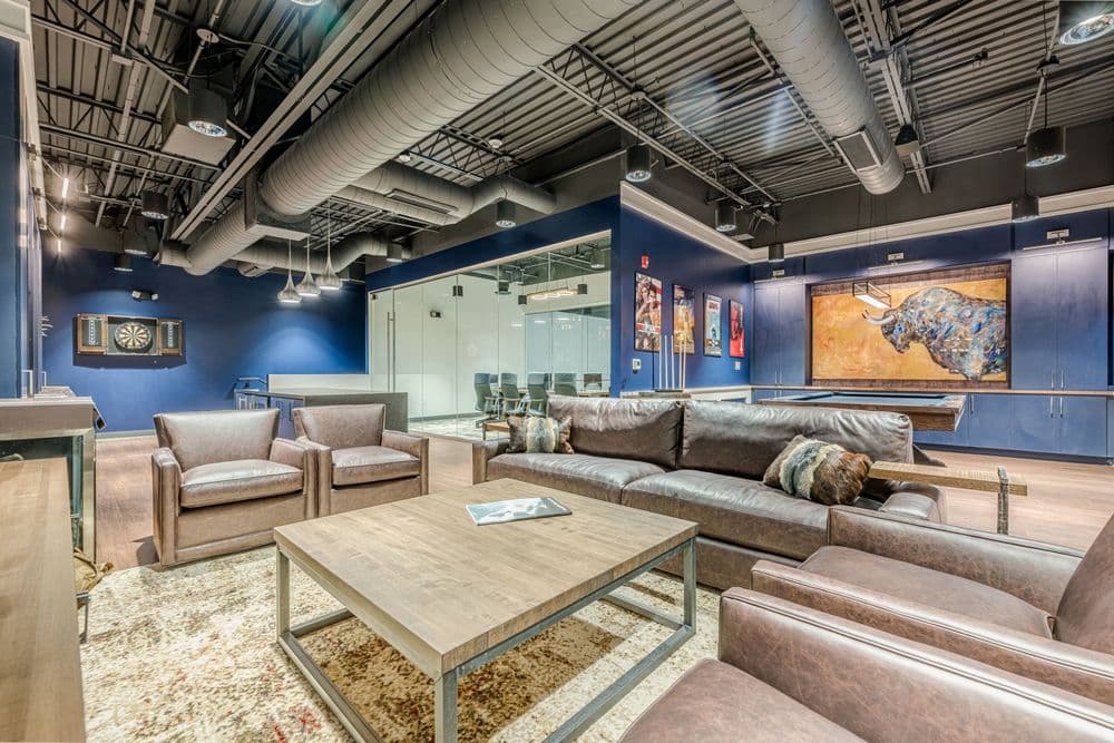Modern lounge area with leather seating, dartboard, and colorful wall art in corporate office.