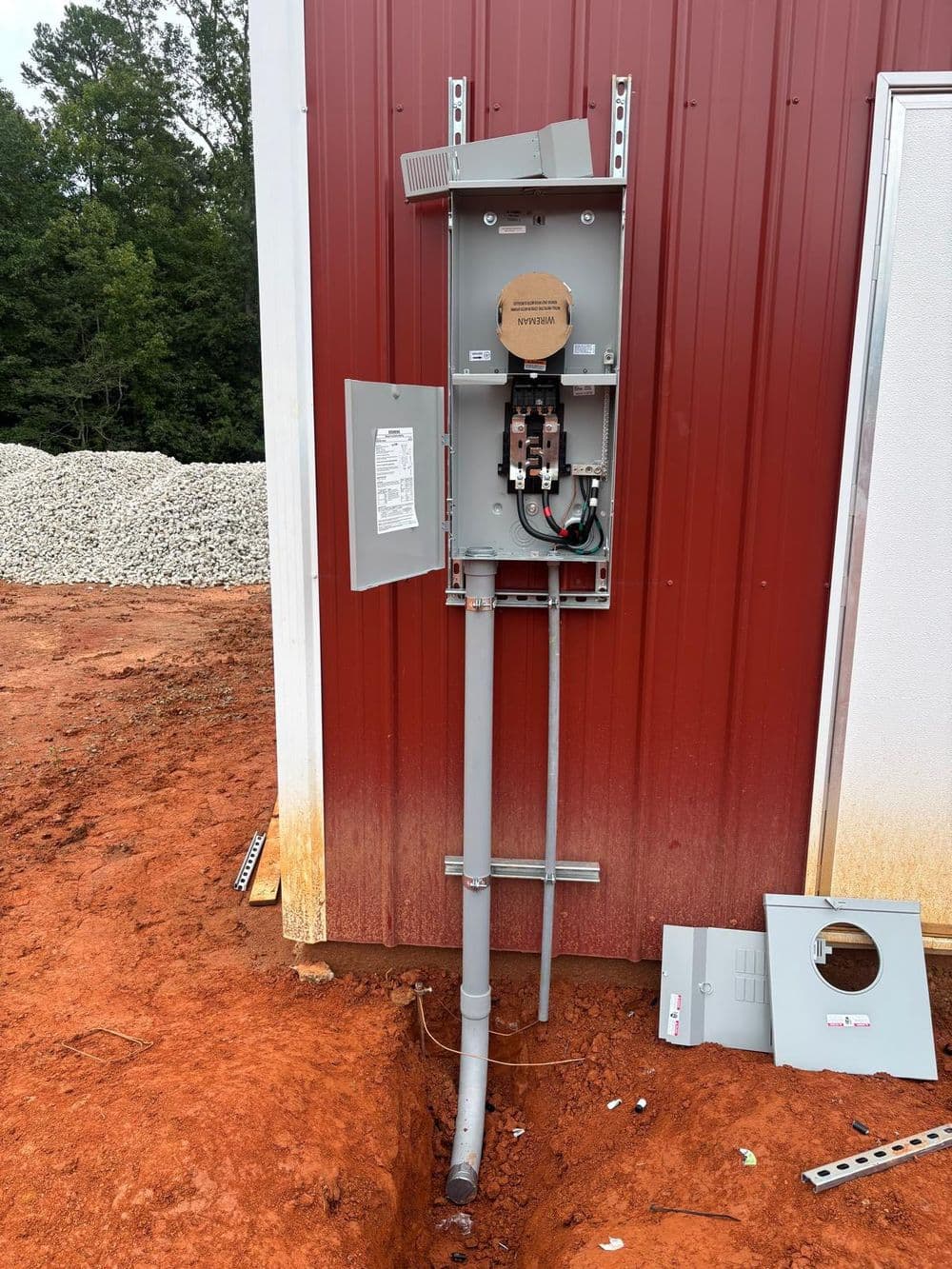 Electric meter box mounted on a red shed, with conduit and removed panel on the ground.