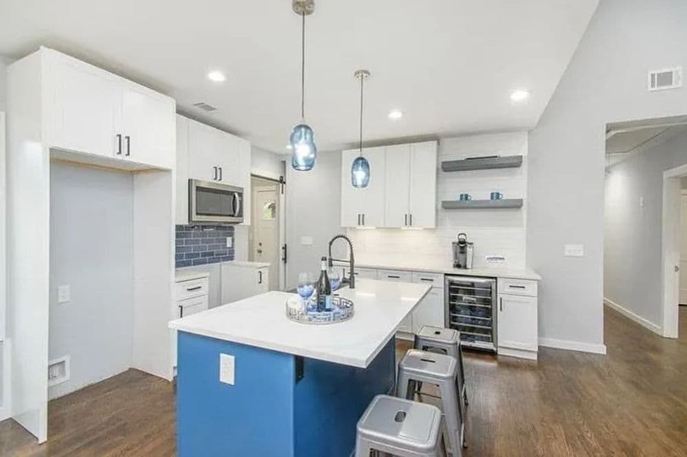 Modern kitchen with white cabinets, blue island, pendant lighting, and stainless steel appliances.
